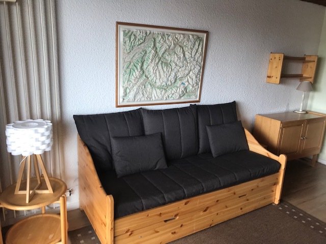 Et hyggeligt stuehjørne med en daybed i træ med mørke hynder, der minder om en afslappende sommerferie i Østrig. Over sengen hænger et indrammet topografisk kort på væggen. Til venstre et rundt sidebord med hvid lampe og til højre et træskab med en lampe på toppen.
