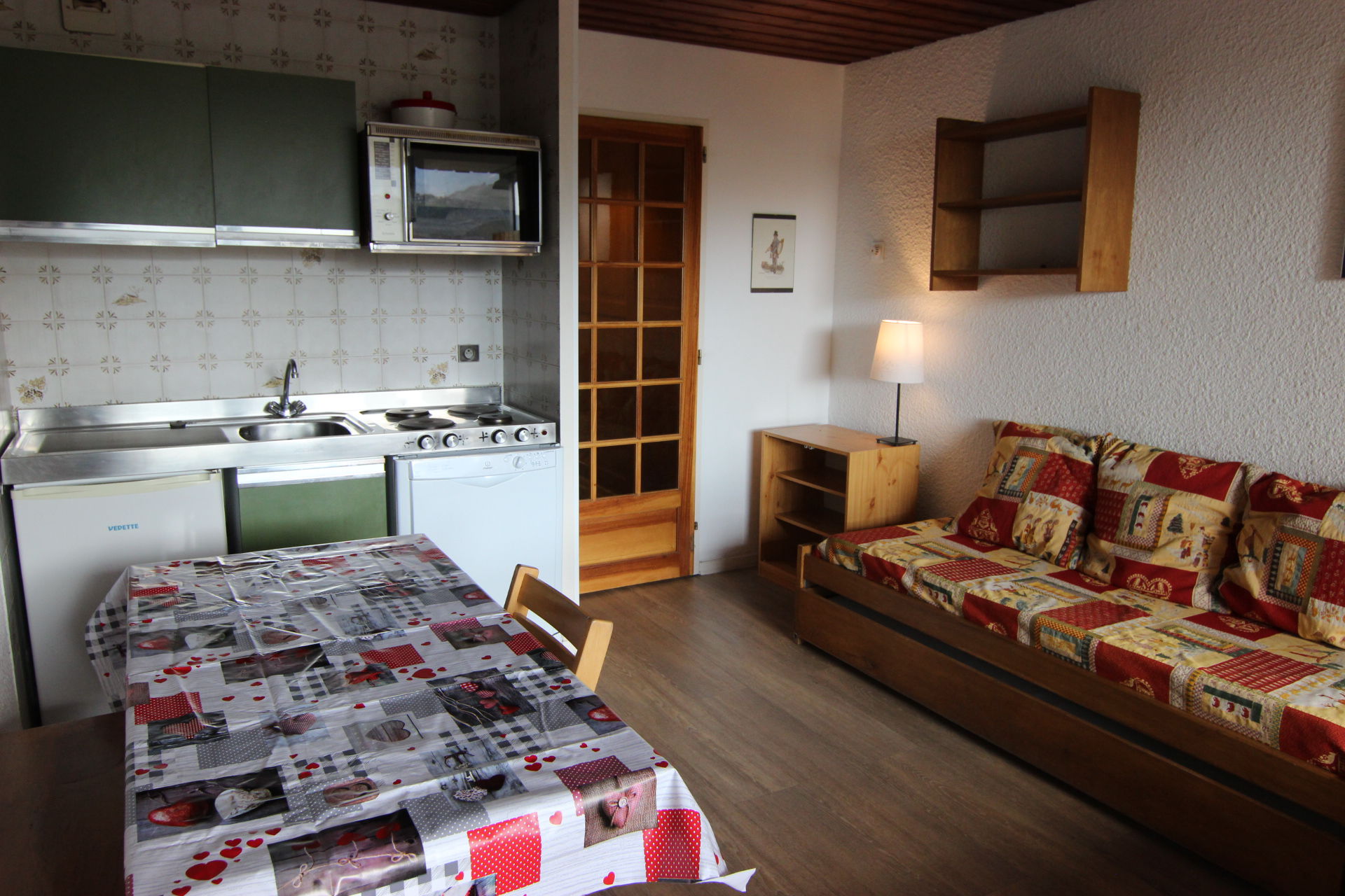 Et hyggeligt køkken og opholdsstue i Saalbach med et grønt og hvidt tekøkken med komfur, vask og mikroovn. Der er en farverig mønstret sofa, trædør, lampe, lille bord med printet dug og hylder - et perfekt tilflugtssted efter eventyrlige skirejser.