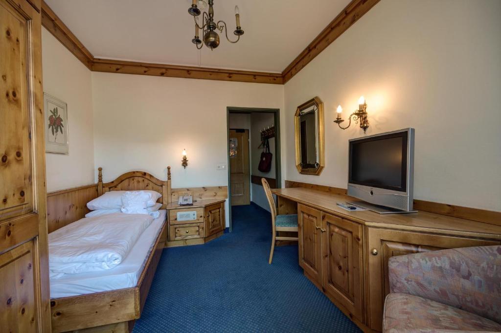 Et hyggeligt hotelværelse med en enkeltseng, træmøbler, et tv på et skab, et skrivebord med en stol, et vægspejl og blød belysning fra væglampetter. Værelset har blåt tæppe og cremefarvede vægge.