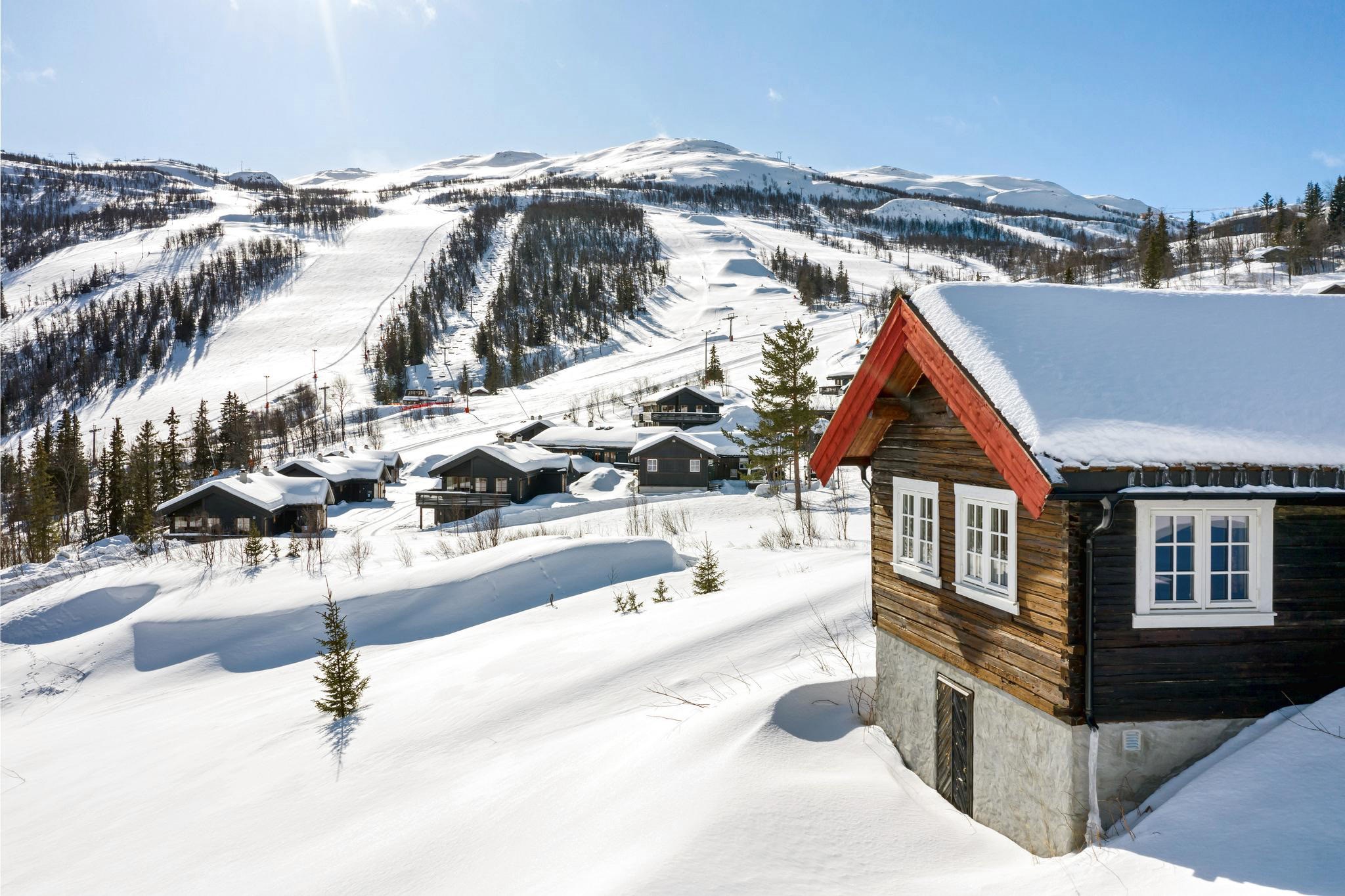 Et snedækket bjerglandskab med træhytter spredt ud over bjergsiden i Westendorf. Den ene hytte er i forgrunden med snedækkede tage, sat mod skiløjper og en klar blå himmel på en solrig skiferiedag.