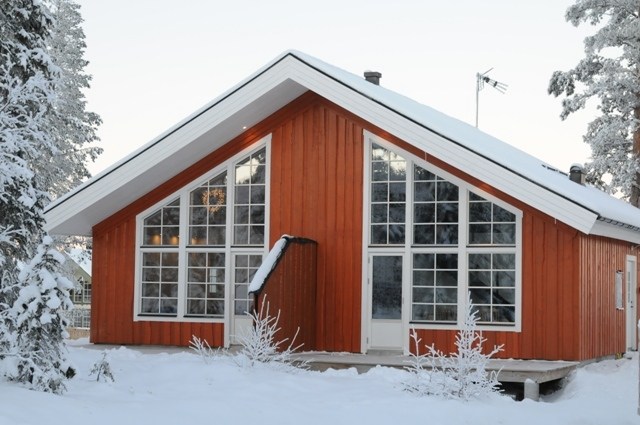 En moderne rød hytte med store trekantede vinduer står omgivet af snedækkede træer i Wagrain. Det let spidse tag, toppet med en antenne, supplerer den fredfyldte vinterscene, mens sne dækker jorden.