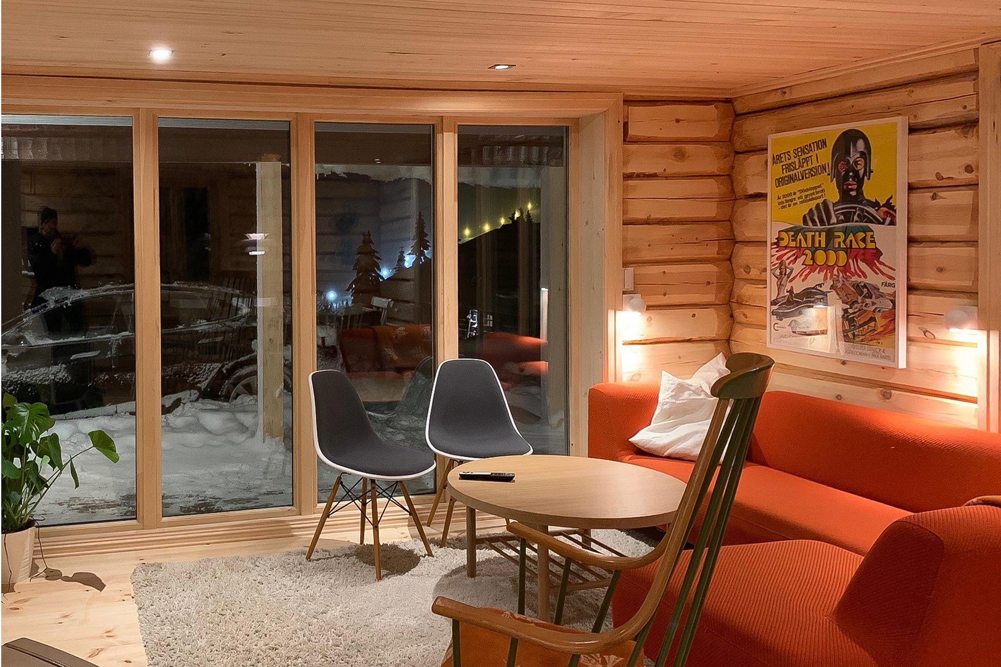 En hyggelig træstue med et stort vindue byder på sneklædte udsigter, der minder om Westendorf. Indeni skaber to moderne stole, en orange sofa, et lille sofabord og en gyngestol varme. En Death Race 2000 plakat tilføjer karakter til væggen.
