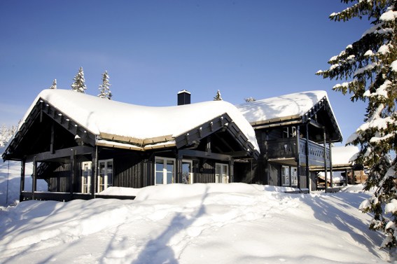 En sort træhytte med et stejlt, snedækket tag ligger roligt i et snelandskab omgivet af træer, der minder om et hyggeligt tilflugtssted, du måske finder i Saalbach. Dens veranda og store vinduespartier inviterer dig til at nyde den klare blå himmel, der fuldender disse idylliske skiferie rammer.