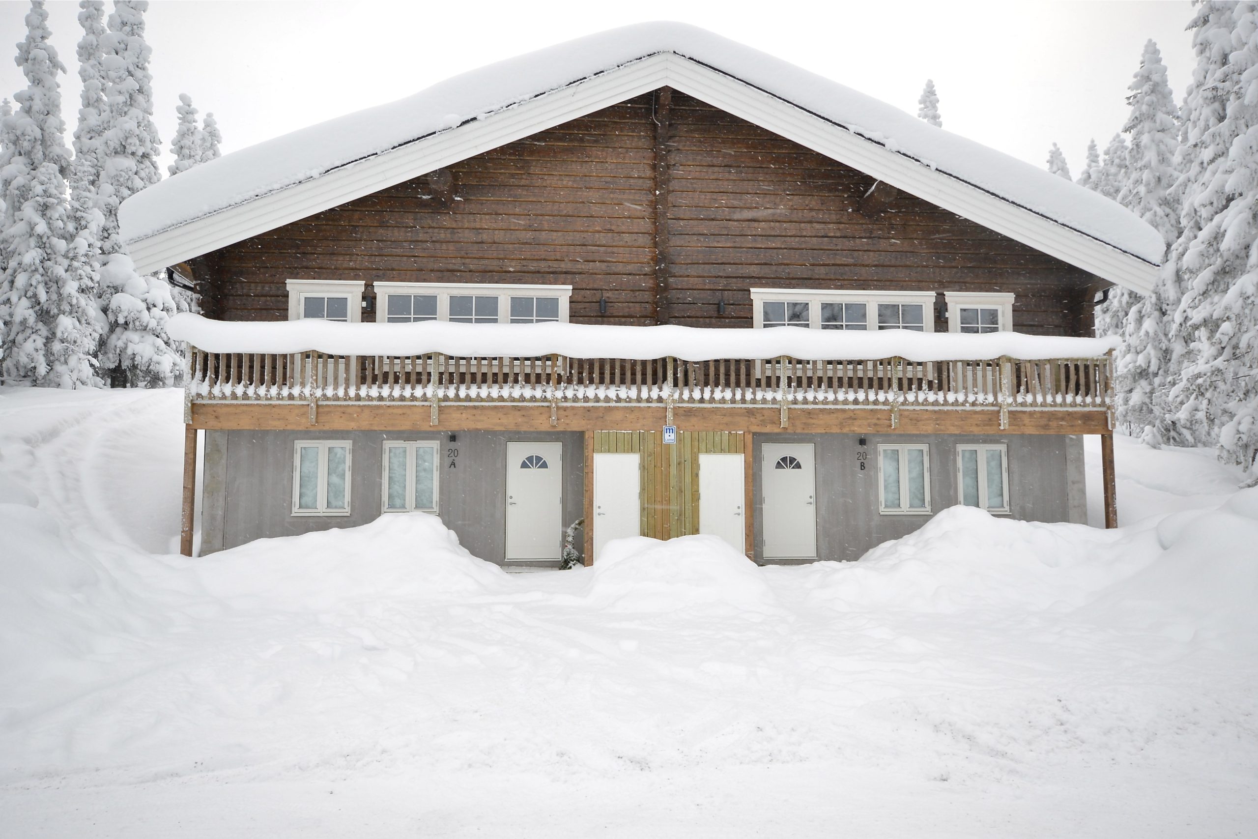En snedækket træhytte med et skrånende tag og flere døre ligger i et fredfyldt Westendorf-vinterlandskab. Omgivet af snefyldte træer fanger scenen et fredeligt skiferiemiljø.