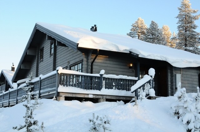 En hyggelig træhytte i Saalbach, dækket af sne og beliggende i et snelandskab med træer i baggrunden, byder på en fredfyldt vinterscene under en klar blå himmel. Det er et idyllisk sted for skiferie- og skirejseentusiaster, der søger ro midt i den uberørte skønhed.