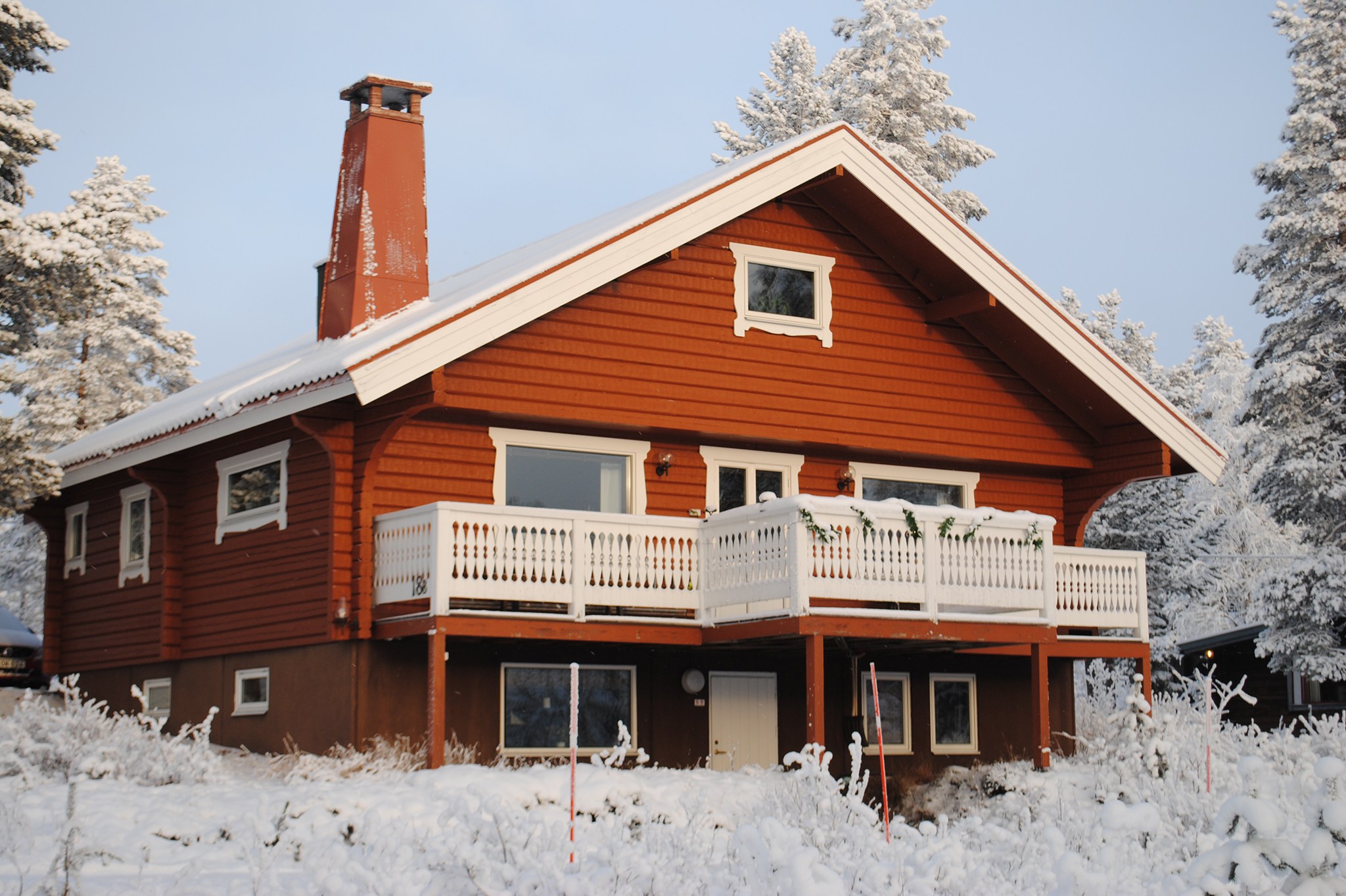 En hyggelig rød træhytte med en hvid balkon ligger omgivet af snedækkede træer og fanger essensen af en rolig vinterscene. Dette idylliske tilflugtssted er perfekt til en skiferie nær Saalbach, hvor taget og jorden er smukt dækket af uberørt sne.