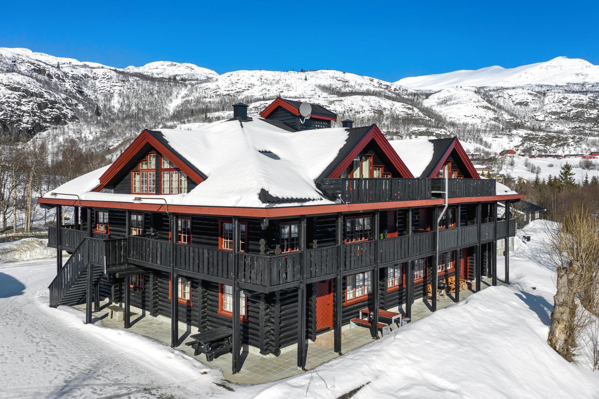 En stor træhytte med et sort ydre og røde accenter er omgivet af sne, der afspejler Westendorfs charme. Bygningen har flere vinduer og en omsluttende balkon. Snedækkede bjerge og en klar blå himmel maler den perfekte kulisse for uforglemmelige skirejser.