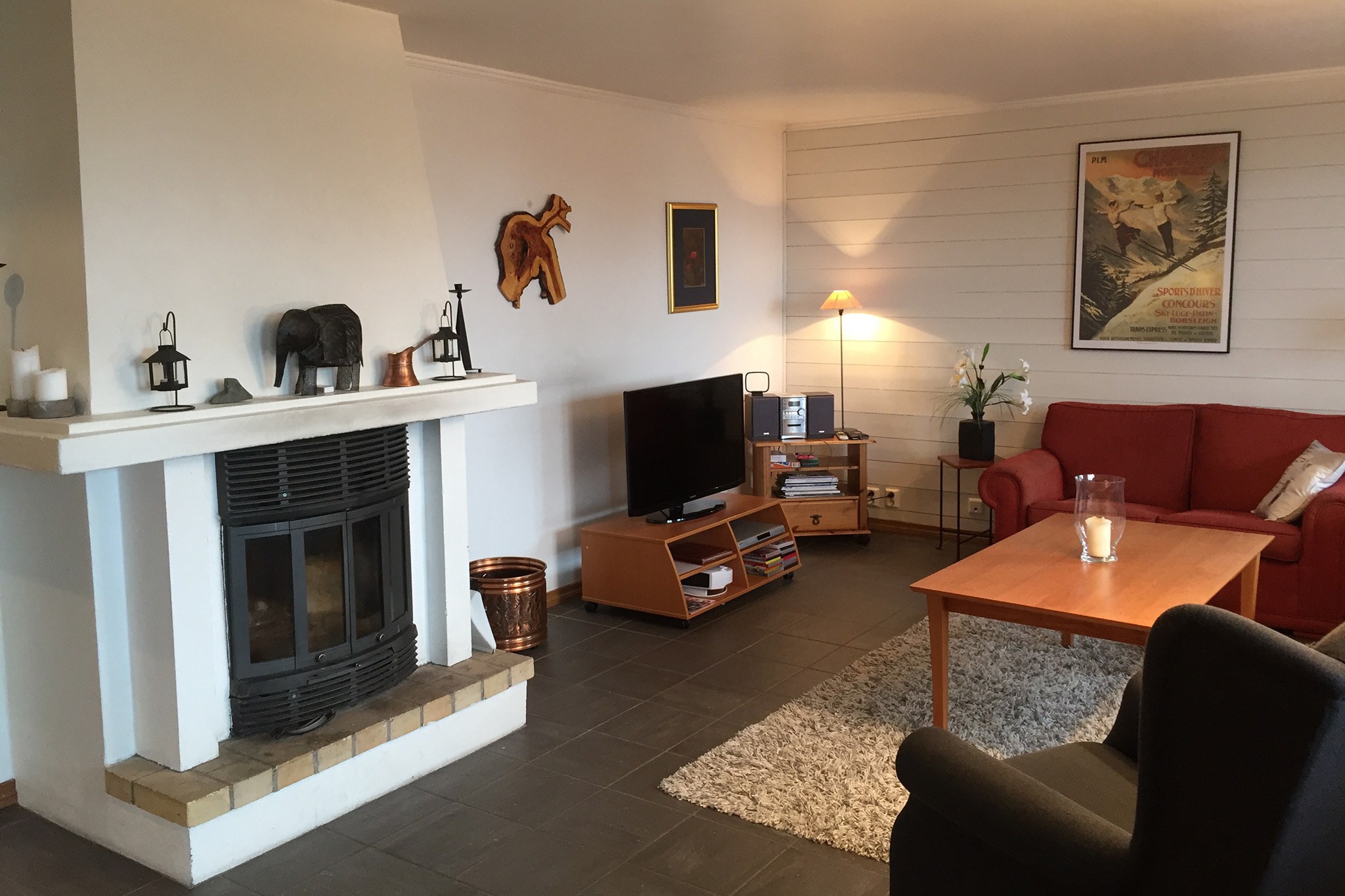En hyggelig stue med pejs, en rød sofa og et sofabord i træ fremkalder charmen ved Wagrain. Udsmykket med kunst og en plakat med naturtema afspejler den roen i sommerferie Østrig. De moderne omgivelser har et overdådigt tæppe og omgivende belysning for varme.