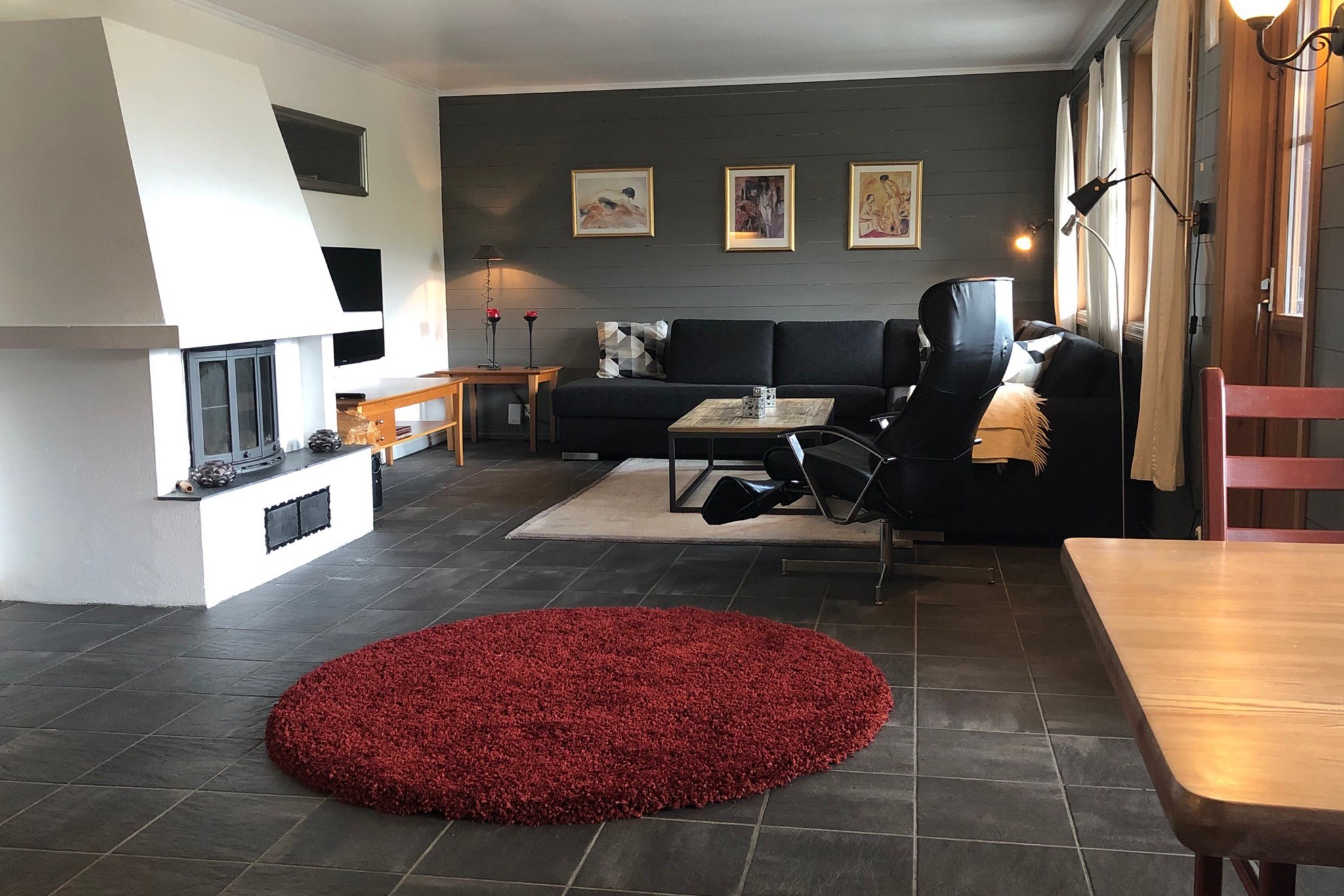 En hyggelig stue i Saalbach har en hvid pejs, sort sofa og en sort lænestol. Et rødt cirkulært tæppe varmer det mørke klinkegulv. Væggene er prydet med indrammet kunst, og et stort vindue byder velkommen til naturligt lys, der minder om de lyse somre i sommerferie Østrig.