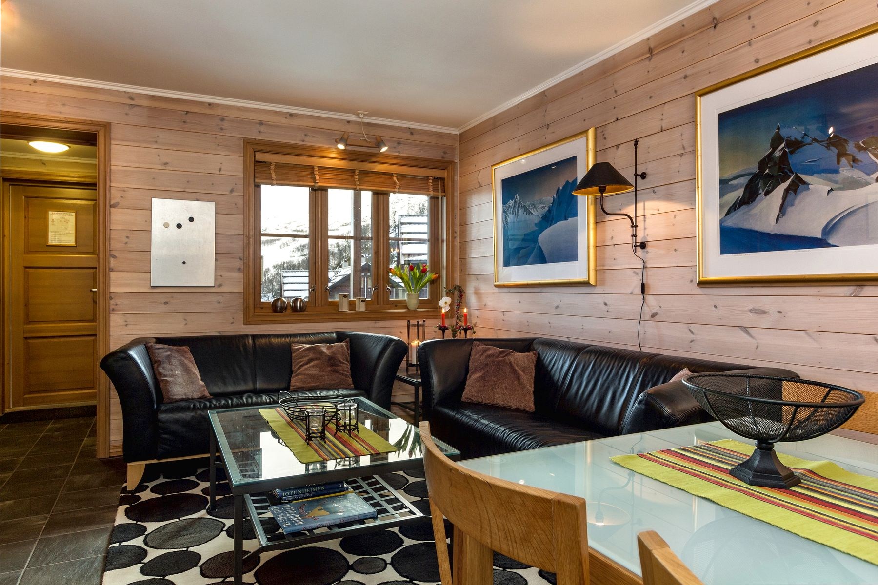 En hyggelig stue med vægge med træpaneler og to lædersofaer har udsigt over det sneklædte Westendorf-landskab. Værelset byder på moderne kunst, et sort/hvidt tæppe, et træbord og en dekorativ skål på en glasoverflade, perfekt til at nyde din skiferie med stil.