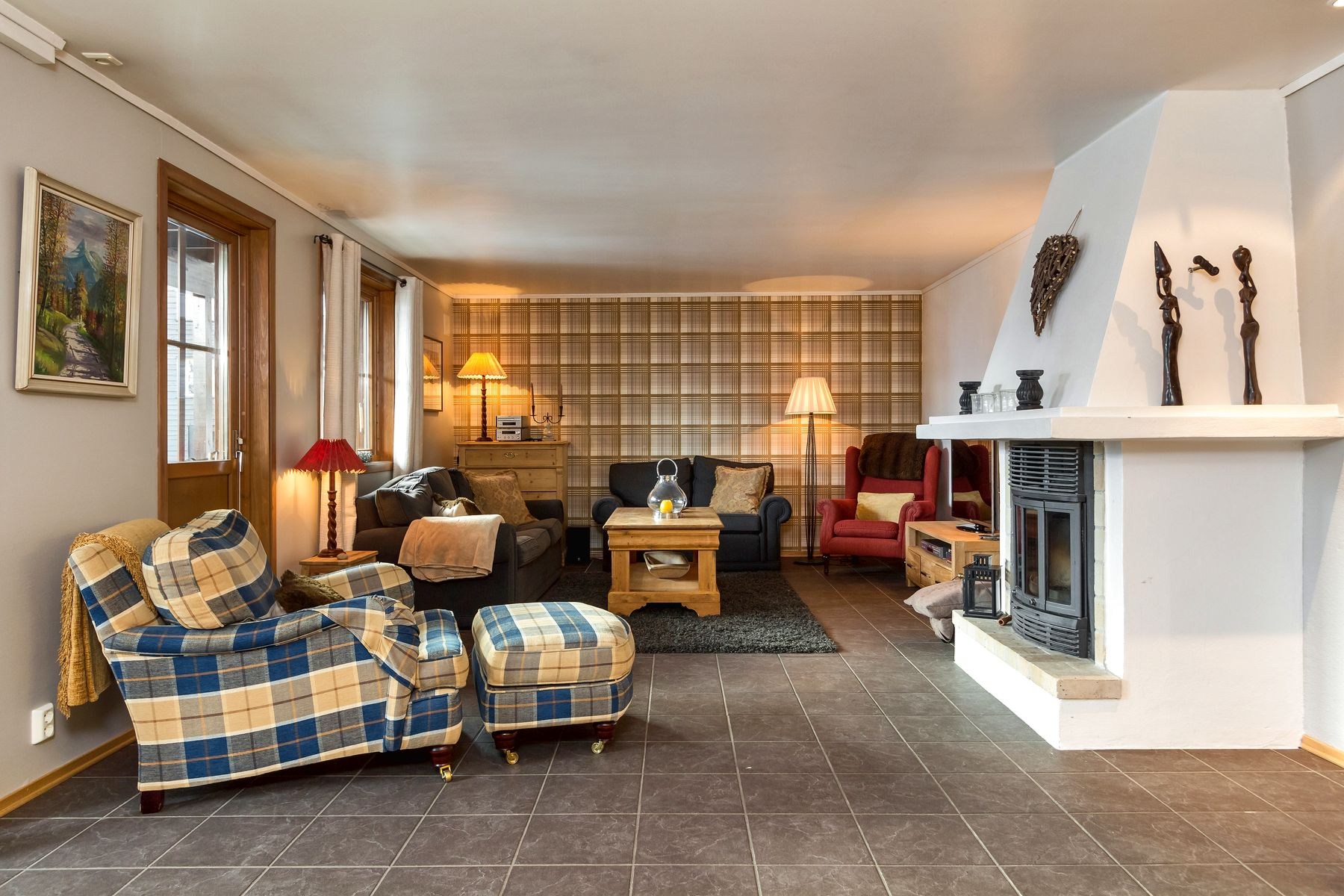 En hyggelig stue i stil med et Westendorf-retræte, med en plaid lænestol, træsofabord og en blanding af moderne og klassisk indretning. Rummet omfatter en stor hvid pejs, to lænestole, lamper og vægkunst, perfekt til at mindes om sidste sommerferie Østrig.