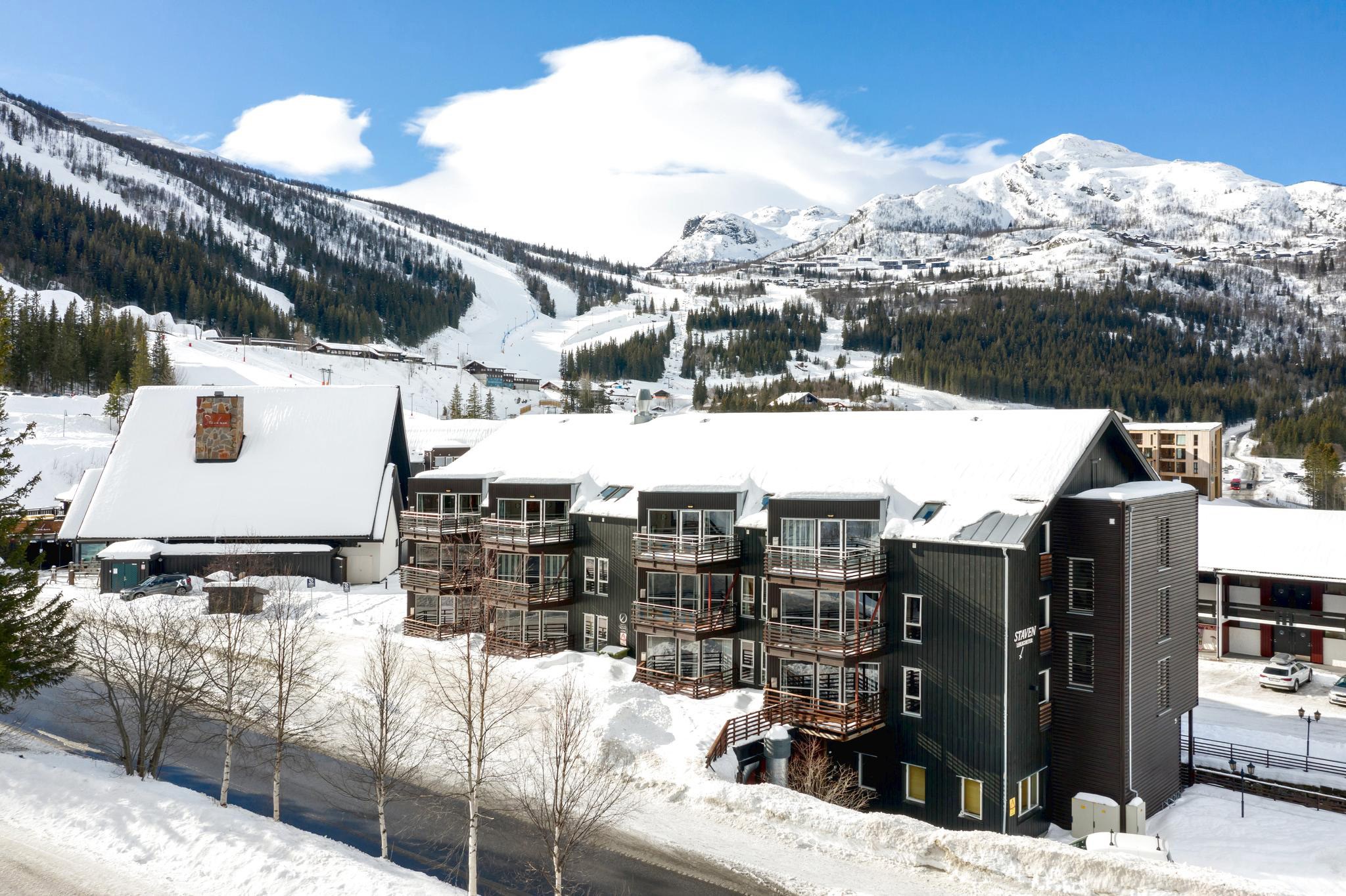 Oplev det naturskønne sneklædte bjergresort Saalbach, hvor moderne sorte og hvide bygninger komplementerer de snedækkede tage, træer og bakker. Med en klar blå himmel og synlige skiløjper i baggrunden er det en perfekt destination for din næste skiferie.