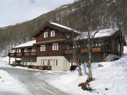 En stor træbygning i chalet-stil med snedækkede tage står majestætisk midt i det sneklædte landskab i Saalbach. Strukturen er omgivet af nøgne træer og kan prale af flere vinduer og en stenbund, sat på baggrund af en bjergskråning, der vækker minder om sommerferie Østrig.
