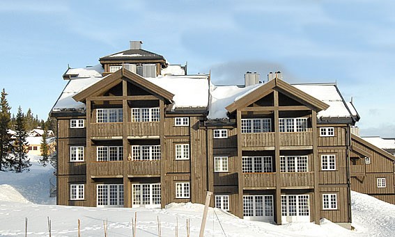 En stor træbygning i chaletstil med flere vinduer og snedækkede tage, beliggende i maleriske Saalbach. Den klare blå himmel tilføjer en fantastisk kulisse til dette vintervidunderland.