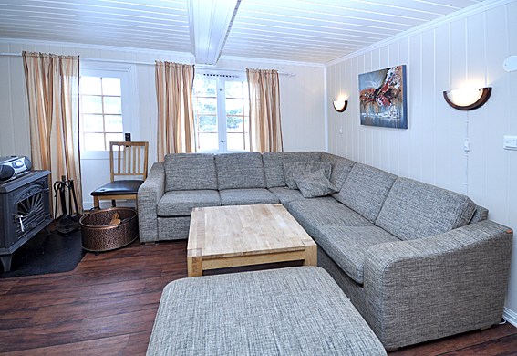 I hjertet af Westendorf har denne hyggelige stue en grå L-formet sofa, et sofabord i træ og en matchende skammel. De hvide vægge kan prale af et maleri og to væglamper. Beige gardiner indrammer vinduer, der byder naturligt lys velkommen, mens en sort brændeovn varmer hjørnet.