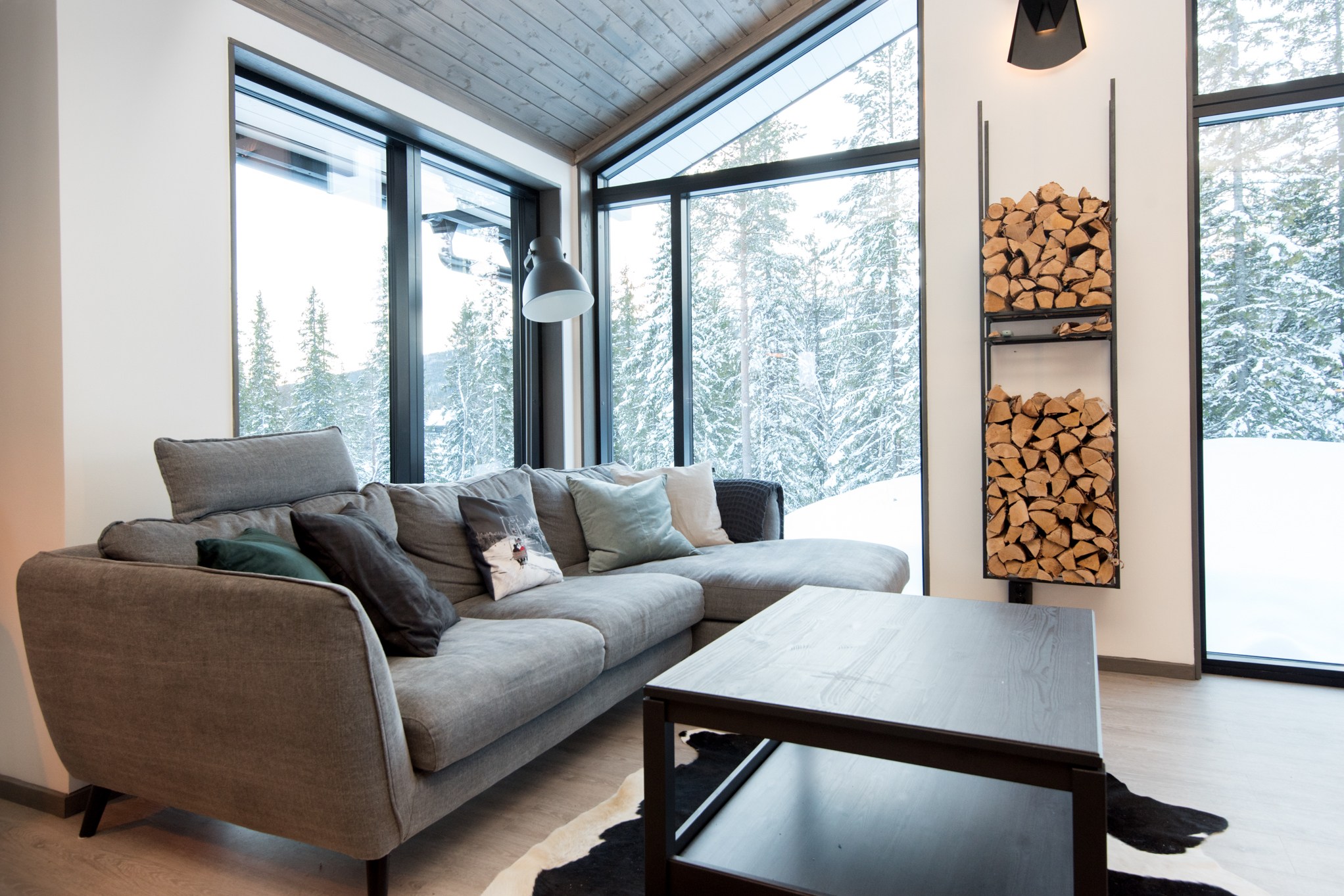 En hyggelig stue med en stor grå sofa prydet med hynder, et sofabord og en stak brænde danner rammerne for din perfekte skiferie. Store vinduer afslører Westendorfs sneklædte skove udenfor, fylder rummet med naturligt lys og inviterer eventyrlysten ind.
