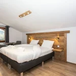 Et minimalistisk soveværelse i Saalbach har en dobbeltseng med en rustik hovedgærde og loft i træ. Det sprøde hvide sengetøj og de foldede håndklæder inviterer dig ind efter en dag med skiferie. Ved vinduet, med et gardin, sidder et lille bord og en stol, mens trægulvet fuldender dette hyggelige tilflugtssted.