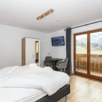 Et moderne hotelværelse med en pænt lavet dobbeltseng, et lille bord med to stole, et klædeskab og et væghængt tv. Store glasdøre åbner ud til en balkon med udsigt over fantastiske bjergrige landskaber - de perfekte rammer for dit skiferieeventyr. Trægulve forstærker rummets hyggelige fornemmelse.